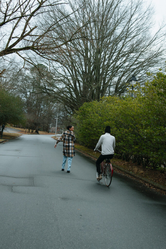 couple riding down the street. girlfriend is running infront of boyfriend while he is on the bike.